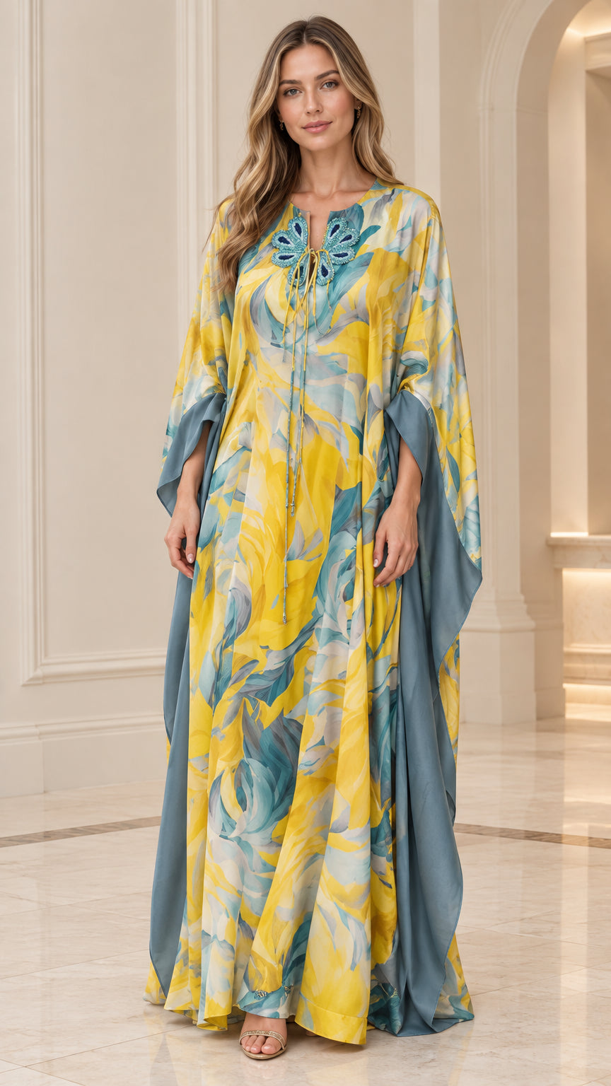 Front view of woman wearing yellow and teal floral caftan maxi dress with butterfly neckline appliqué