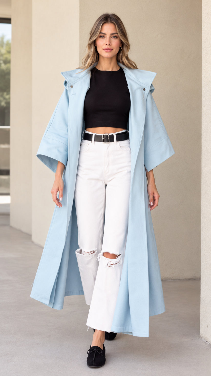 Front view of woman wearing sky blue hooded maxi duster coat over black top and white jeans