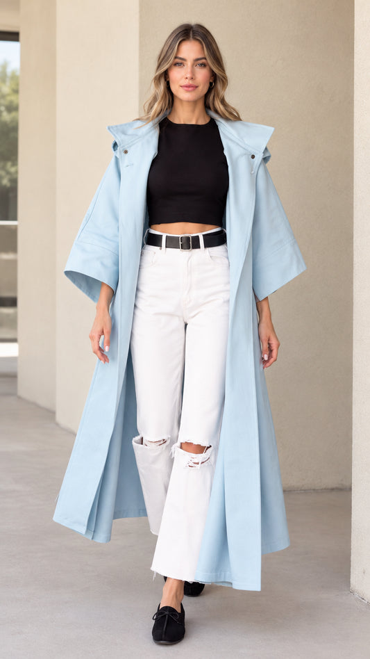 Front view of woman wearing sky blue hooded maxi duster coat over black top and white jeans