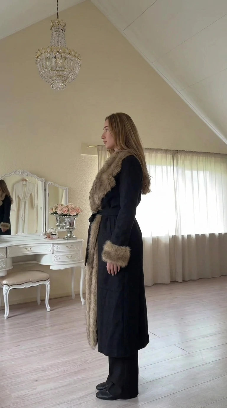 Side profile view of model in Black belted long coat with faux fur collar and cuffs