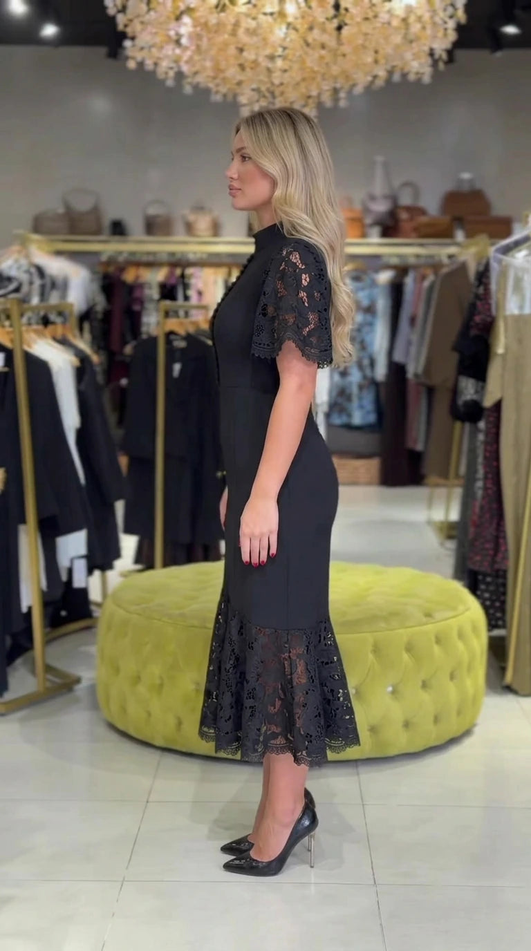Side profile view of black mock neck lace midi dress showing slim mermaid contour
