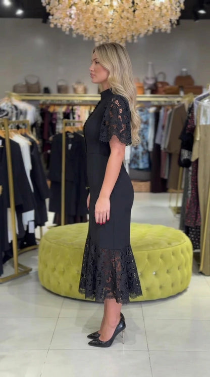 Side profile view of black mock neck lace midi dress showing slim mermaid contour