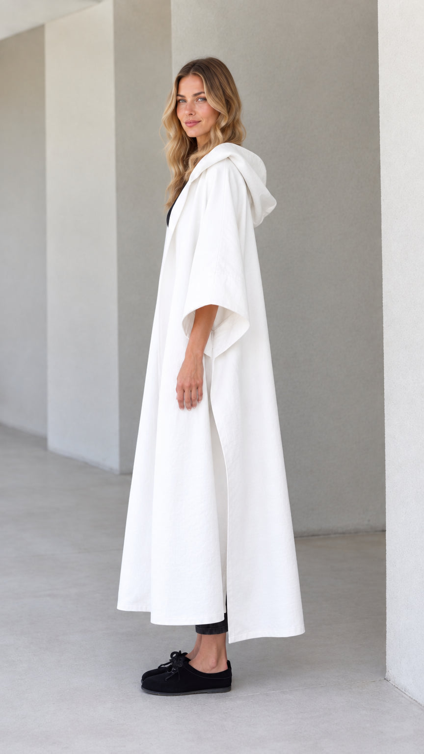 Side profile view of model wearing white hooded canvas cape duster