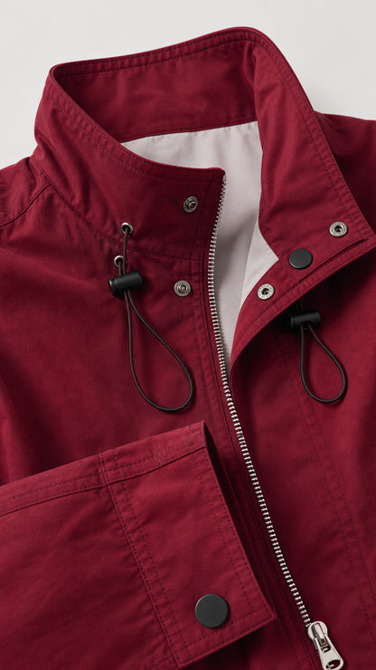 Close-up detail of burgundy coat showing stand collar, drawstrings, zipper, and snap cuff