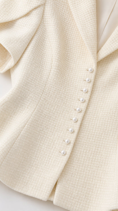 Close-up detail of textured ivory tweed fabric and faux pearl buttons on peplum blazer