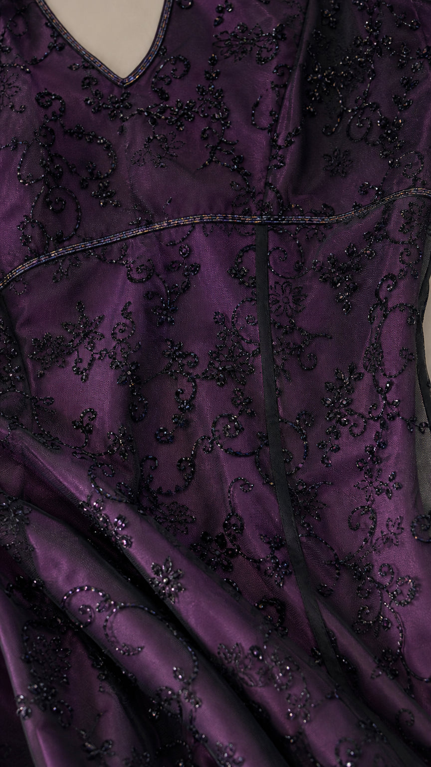 Close-up detail of delicate floral embroidery and beaded texture on deep purple fabric